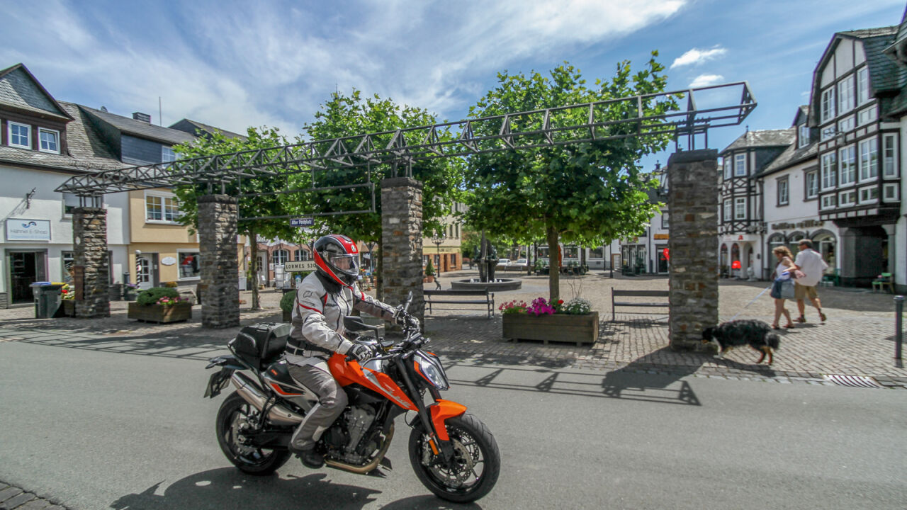 Motorrad auf einem Marktplatz mit Fachwerkhäusern und einer Pergola Motorrad auf einem Marktplatz mit Fachwerkhäusern und einer Pergola